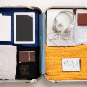 open luggage flat on the floor with ipad, head phones, clothes, yellow sweater, passport, list and travel essentials